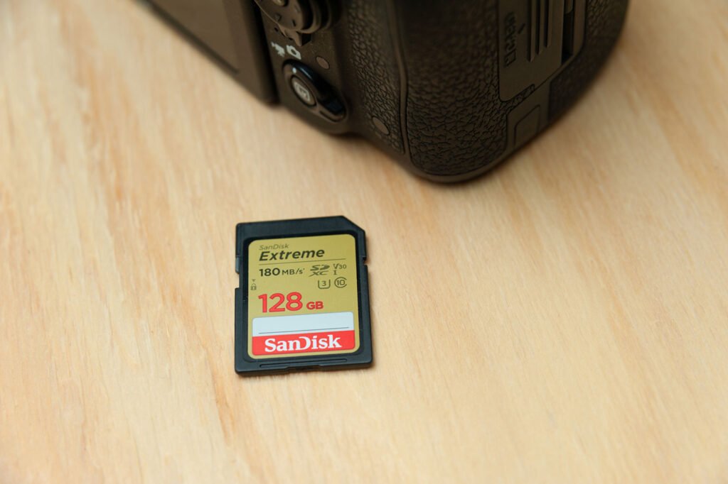 SanDisk Extreme 128GB SD card next to a Nikon camera on wooden surface